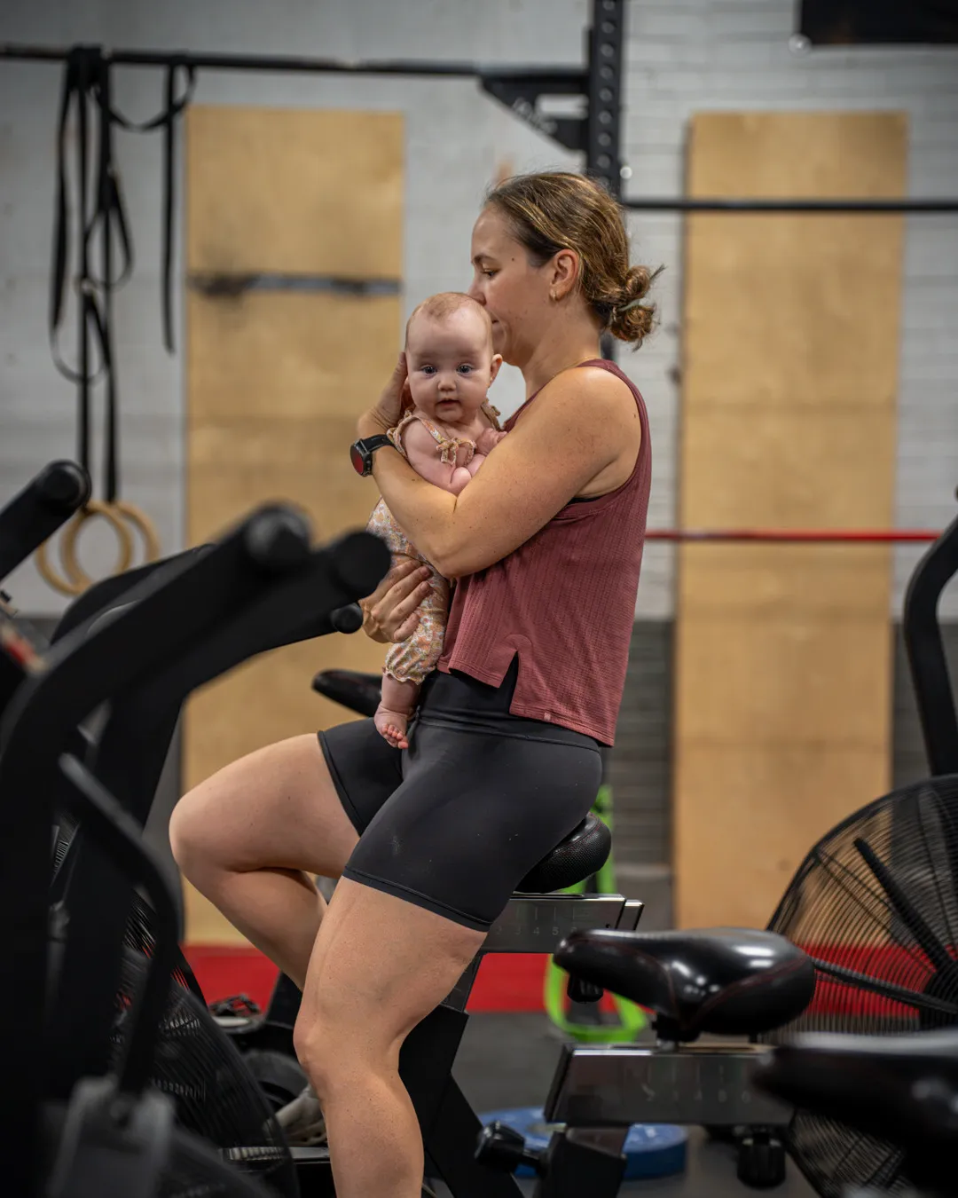 A mom kisses her baby in her arms during her workout at the gym